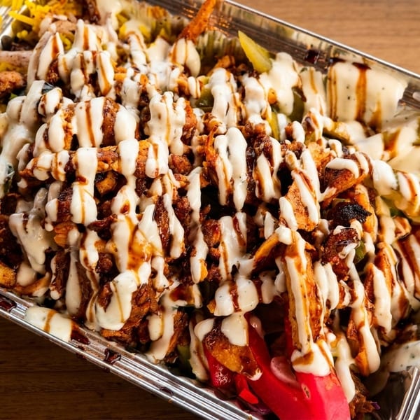 Chicken shawarma platter with white sauce and dark drizzle, served in a foil container.