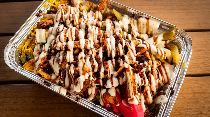 Chicken shawarma platter with white sauce and dark drizzle, served in a foil container.