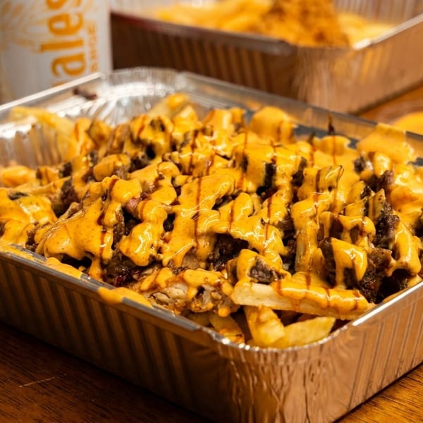 Fries topped with meat and cheese sauce in a foil container on a wooden table.
