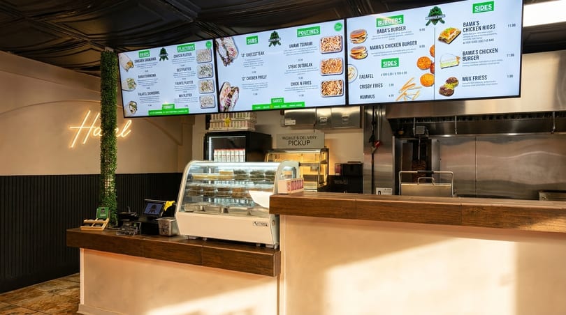 Restaurant counter with a display case, digital menu boards, and a neon "Halal" sign.