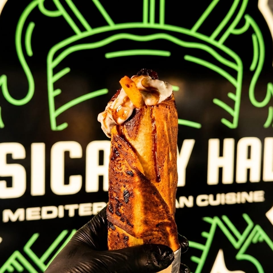 A hand in a black glove holds a dessert wrap topped with cream and fruit in front of a neon sign.